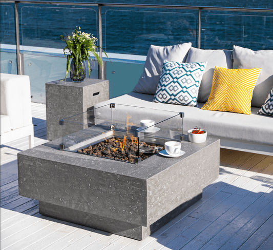 Table brasero Manhattan gris clair posé dans un salon extérieur au sol blanc